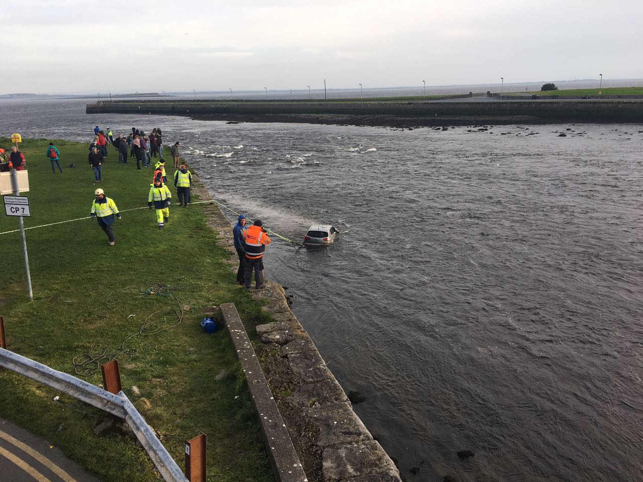 Passersby and emergency services gather on the Long Walk to watch the car as it is dragged from the Corrib